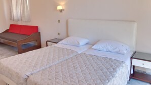 A bedroom with two beds, a nightstand, a lamp, and a red cushion on a bench. - Tarra Seaside Hotel (Apokoronas)