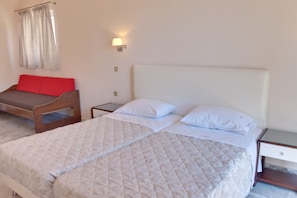 A bedroom with two beds, a nightstand, a lamp, and a red cushion on a bench. - Tarra Seaside Hotel (Apokoronas)