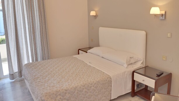 A hotel room with a bed, a nightstand, a lamp, and a window with curtains. - Tarra Seaside Hotel (Apokoronas)