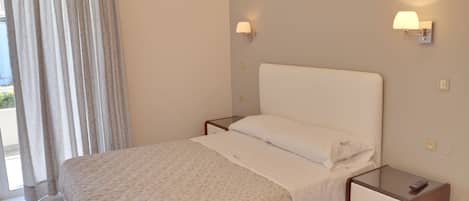 Una habitación de hotel con una cama, una mesita de noche, una lámpara y una ventana con cortinas.