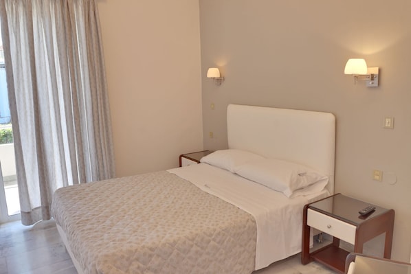 A hotel room with a bed, a nightstand, a lamp, and a window with curtains. - Tarra Seaside Hotel (Apokoronas)