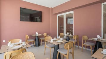 Un comedor con varias mesas y sillas, un televisor de pantalla plana montado en la pared y un ventanal corredero que da a otra habitación.