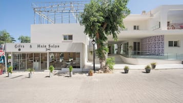 Un salón de belleza con un letrero visible, un árbol en primer plano y un edificio moderno al fondo.