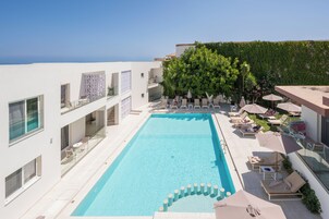 Un hotel moderno con piscina en la azotea, sillones de descanso y vistas al mar.