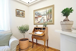 A room with a wooden desk, a potted plant, a painting, and a sofa. - Art Gallery Hotel (Athens)