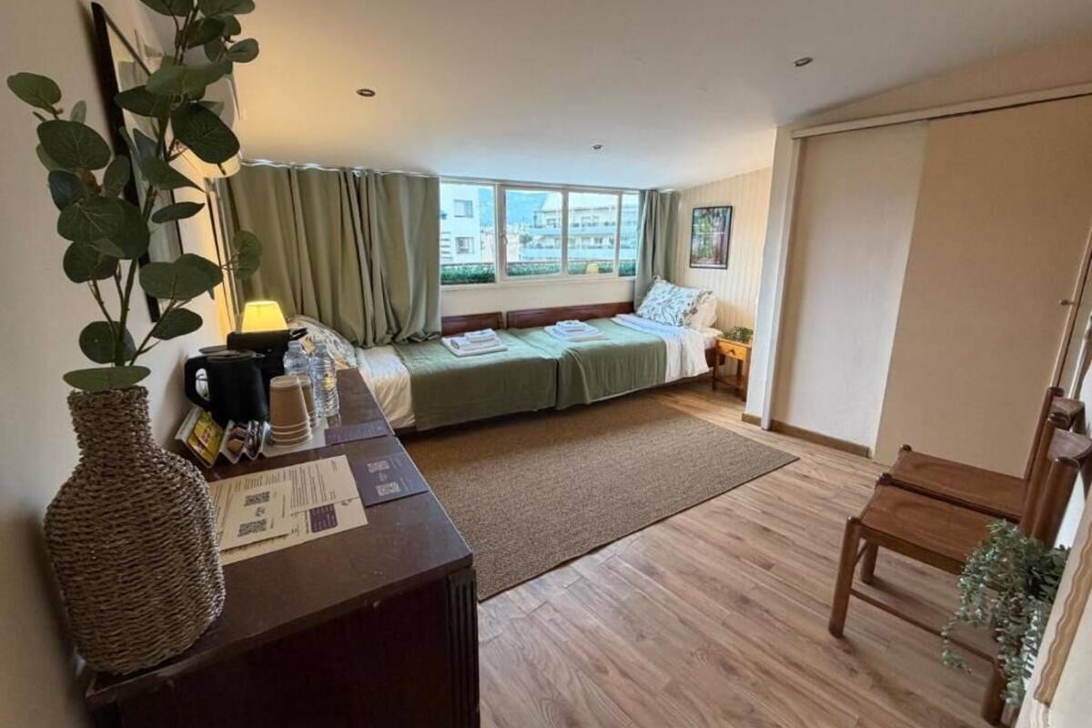 A room with a bed, a desk with a lamp, a vase, and a window with curtains.