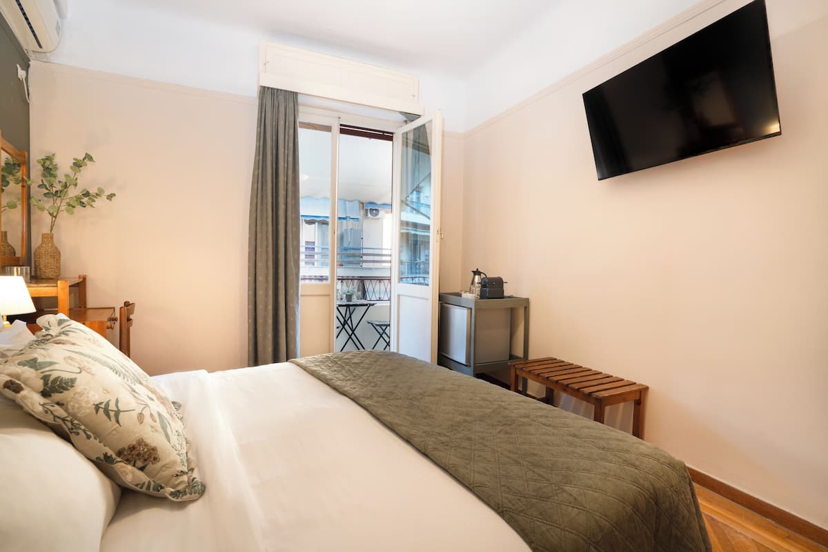 A hotel room with a bed, a TV, a balcony, and a small table.