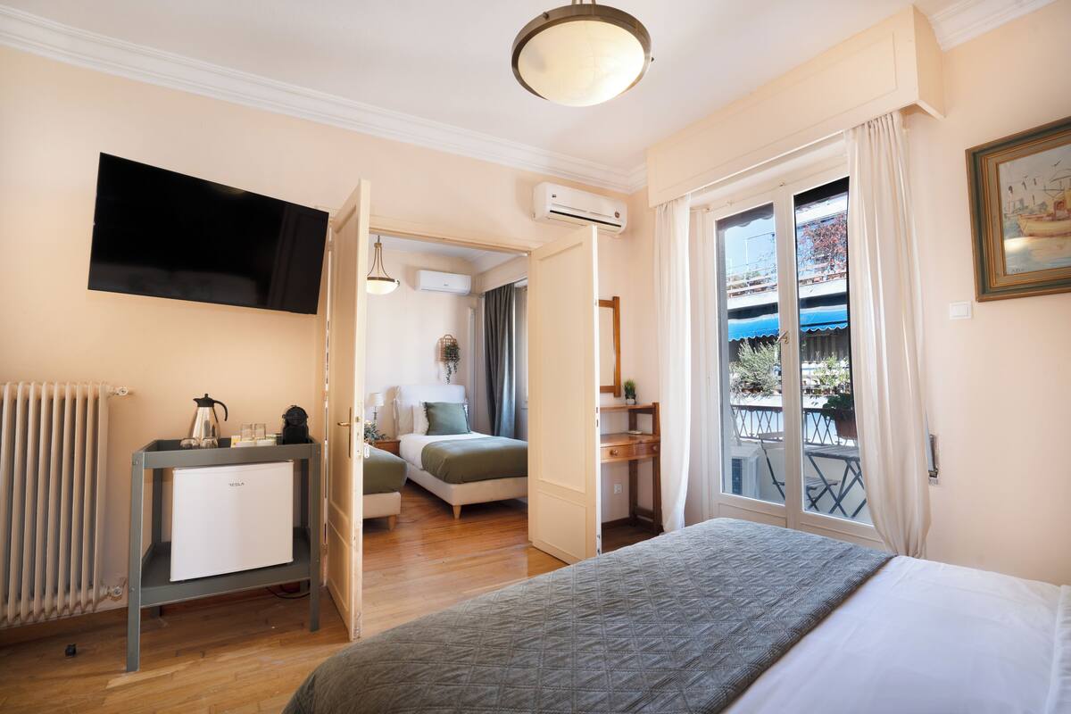 A hotel room with a bed, a desk, a radiator, a TV, and a balcony with a view.