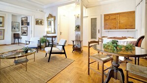 A spacious living room with a round glass coffee table, a dining table with chairs, and a large wooden cabinet. - Art Gallery Hotel (Athens)