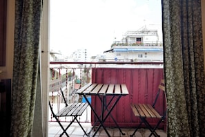 A balcony with two wooden tables and chairs, a red partition, and a view of buildings in the background.