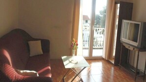 Un salon comprenant un canapé, une petite table avec un vase, un téléviseur posé sur un meuble et une porte-fenêtre coulissante donnant sur un espace extérieur.