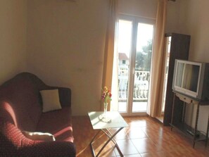 Een woonkamer met een bank, een kleine tafel met een vaas, een televisie op een meubel en een glazen schuifdeur naar een buitenruimte.