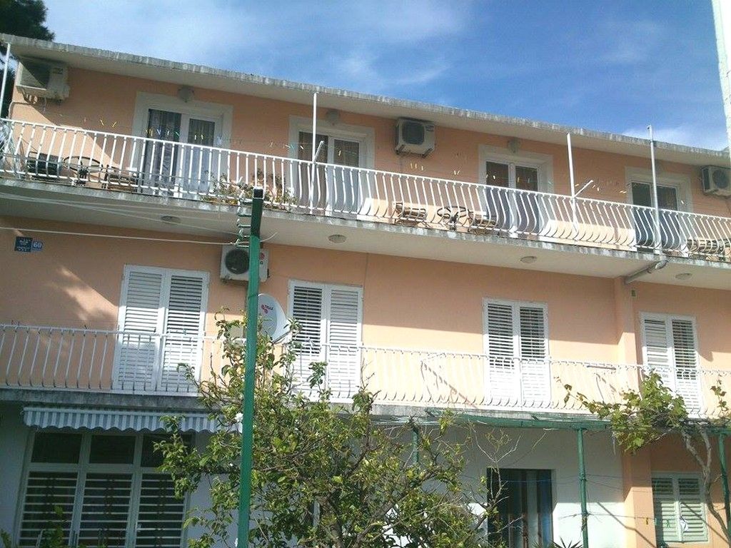 A multi-story building with balconies, windows with shutters, and a clear sky.
