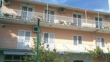 A multi-story building with balconies, windows with shutters, and a clear sky.