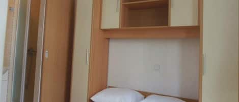 A bedroom with a bed, a wardrobe, and a built-in shelf above the bed.