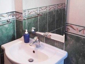 Een badkamer met een wit wastafel, een spiegel en een zeepdispenser.