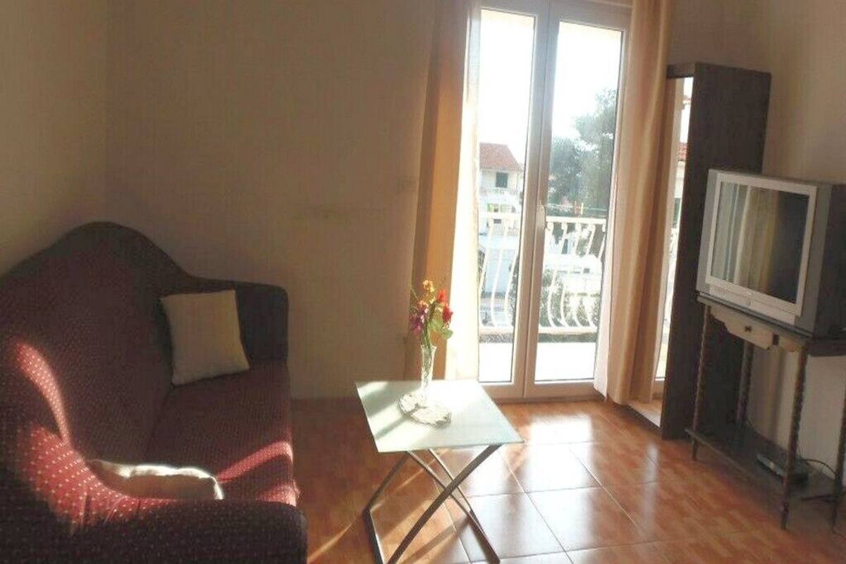 Un salon comprenant un canapé, une petite table avec un vase, un téléviseur posé sur un meuble et une porte-fenêtre coulissante donnant sur un espace extérieur.