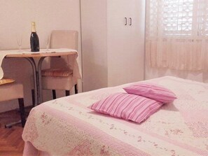 Een kamer met een bed, een stoel, een tafel met een fles en een glas, en een raam met kantgordijnen.