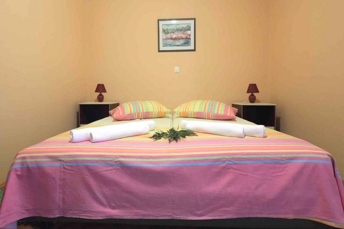 Una cama con colcha a rayas, almohadas y una toalla enrollada. Hay dos mesitas de noche con lámparas.