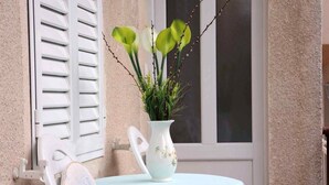 A small balcony with a white chair, a table with a light blue tablecloth, and a white vase with green plants. - Apartments Goran (Makarska)