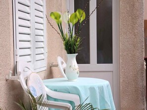 A small balcony with a white chair, a table with a light blue tablecloth, and a white vase with green plants. - Apartments Goran (Makarska)