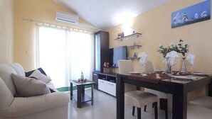 A living room with a sofa, a dining table set for two, and a kitchen area with a TV and cabinets. - Apartments Goran (Makarska)