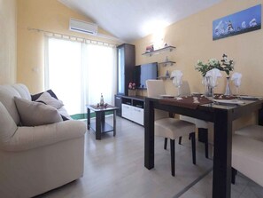 A living room with a sofa, a dining table set for two, and a kitchen area with a TV and cabinets. - Apartments Goran (Makarska)