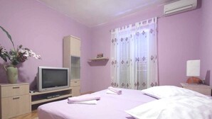 A bedroom with a bed, a television, a cabinet, a window with curtains, and a potted plant. - Apartments Goran (Makarska)