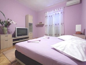 A bedroom with a bed, a television, a cabinet, a window with curtains, and a potted plant. - Apartments Goran (Makarska)