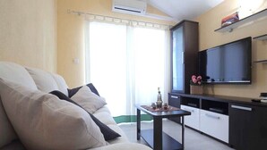 A living room with a sofa, a small table, a TV, and a kitchen area. - Apartments Goran (Makarska)