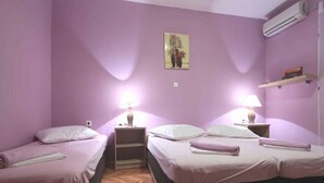 A room with two beds, a wooden floor, a wall-mounted air conditioner, and a small shelf with items. - Apartments Goran (Makarska)