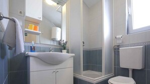 A bathroom with a white sink, mirror, and toilet, a shower enclosure, and a window. - Apartments Goran (Makarska)