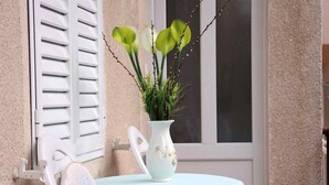 A small balcony with a white chair, a table with a light blue tablecloth, and a white vase with green plants. - Apartments Goran (Makarska)