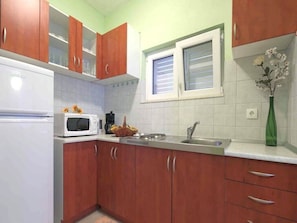Una cocina con armarios de madera, un refrigerador blanco, un microondas, un lavaplatos y una ventana con persianas.