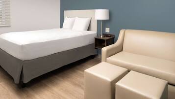 A hotel room with a bed, a nightstand with a lamp, and a sofa.