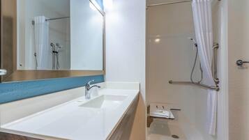 Une salle de bain avec un lavabo blanc, un miroir, une douche avec un rideau blanc et un porte-serviettes.