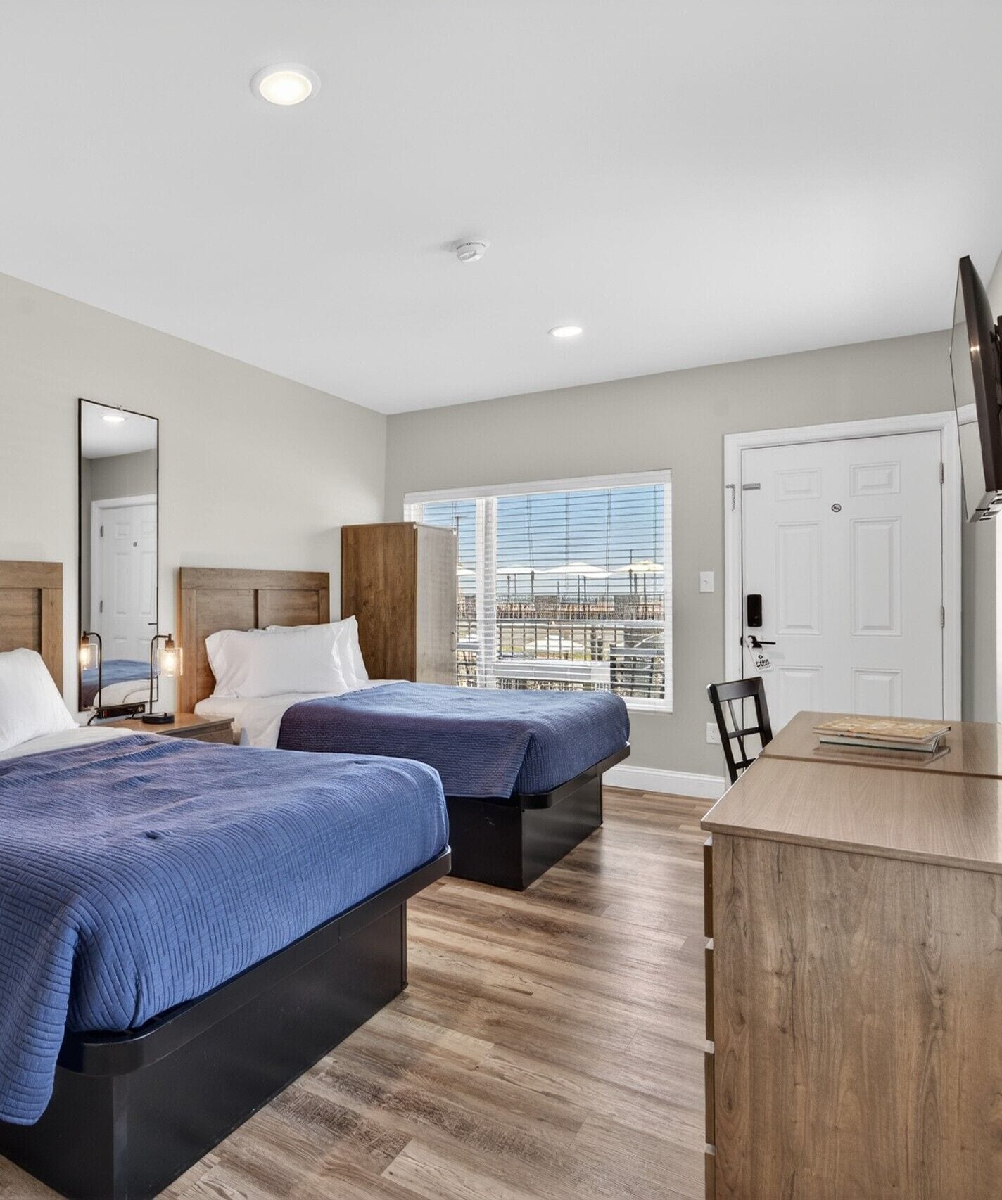Une chambre d’hôtel avec deux lits, un bureau, un miroir et une fenêtre avec des stores.