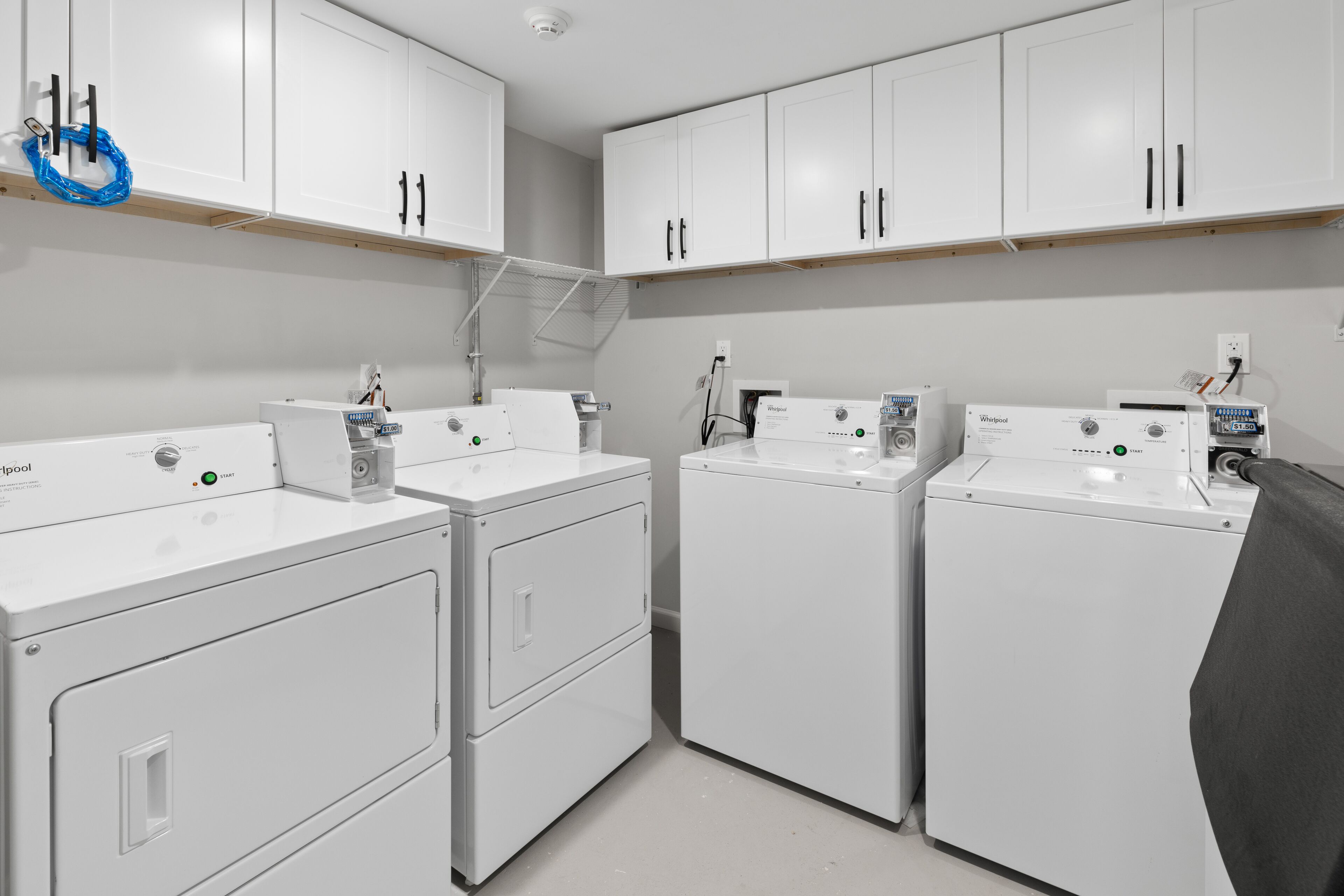 A laundry room with three white Whirlpool washers and dryers, white cabinets, and a blue towel hanging on a rack.