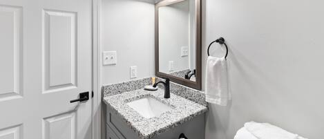 A bathroom with a white door, a sink with a speckled countertop, a mirror with a wooden frame, and a towel rack with a white towel.