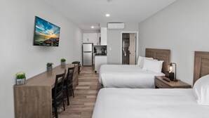 Moderni hotellihuone, jossa on puinen työpöytä, kaksi sänkyä, pieni keittokomero ja taulu, jossa on kuvattuna auringonlasku.