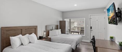 A hotel room with two beds, a wooden headboard, a desk, and a window with blinds.