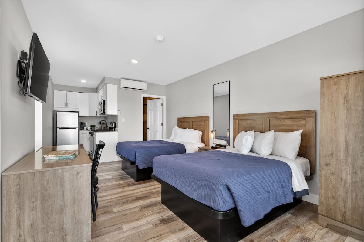 A modern hotel room with two beds, a TV, a kitchenette, and a wooden wardrobe.