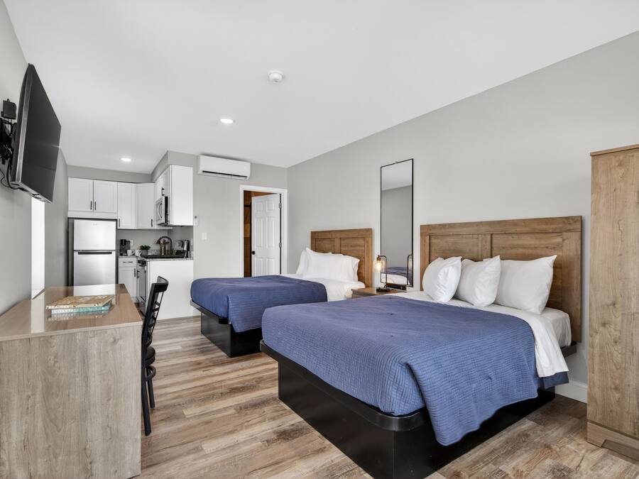 A modern hotel room with two beds, a TV, a kitchenette, and a wooden wardrobe.