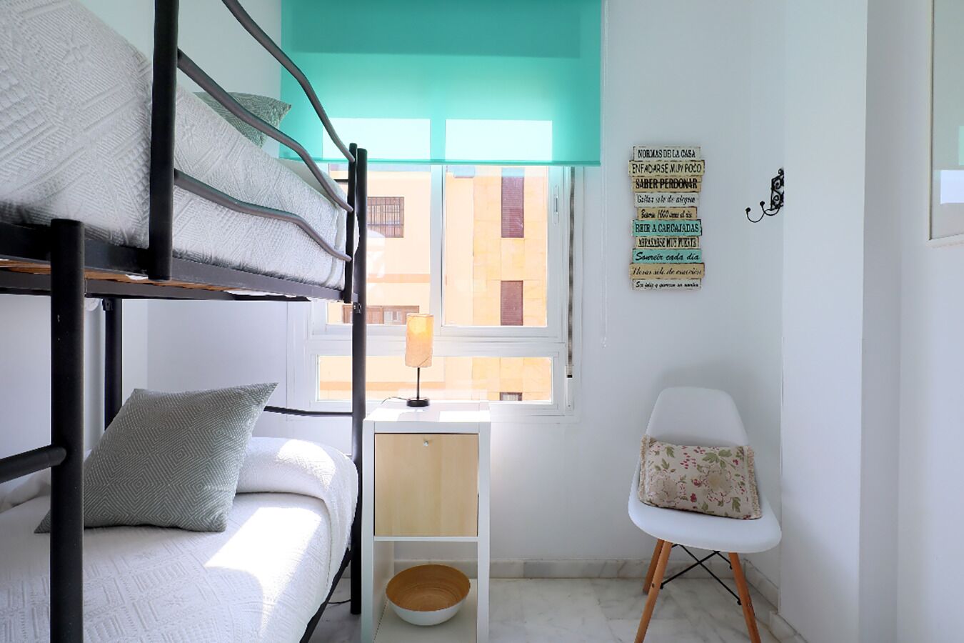 Une chambre de dortoir avec des lits superposés, une petite table avec une lampe, une chaise et une fenêtre donnant sur des immeubles.