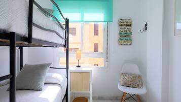 Une chambre de dortoir avec des lits superposés, une petite table avec une lampe, une chaise et une fenêtre donnant sur des immeubles.