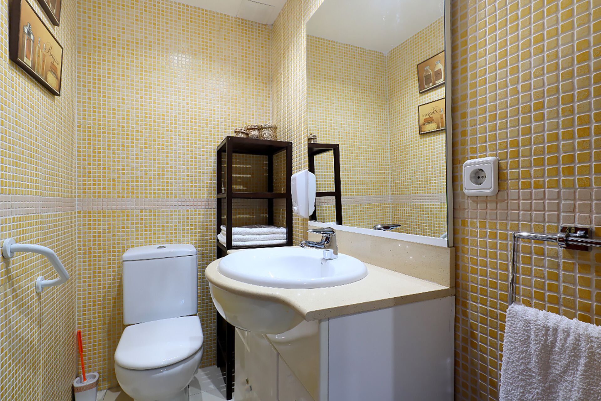 A bathroom with yellow patterned tiles, a white toilet, a sink, and a towel rack.
