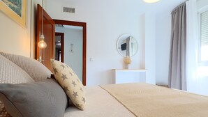 Un dormitori amb llit, una taula de nit, un mirall i una finestra amb cortines.