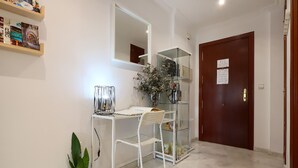 Un passadís amb un escriptori blanc, un mirall, una planta en test i una porta de fusta.