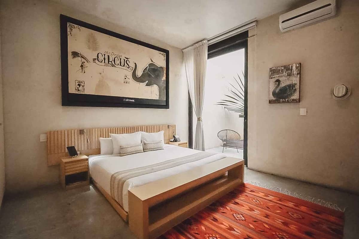 Une chambre à coucher avec un lit, des tables de chevet, un tableau encadré au mur et une fenêtre avec des rideaux.