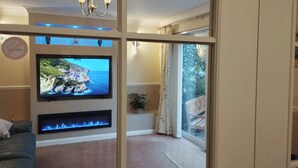 Un salon doté d’un téléviseur à écran plat fixé au mur, d’une cheminée en dessous et offrant une vue sur l’extérieur par une fenêtre.